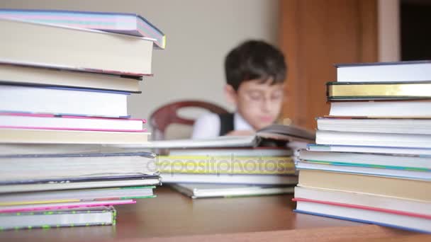 Мальчик сидит за столом с стопкой книг. ребенок читает. мальчик в очках — стоковое видео
