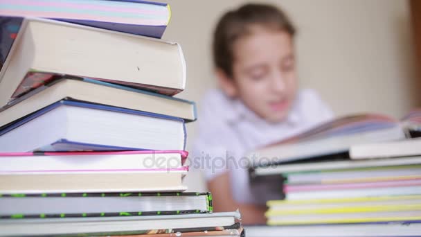 Petite fille en uniforme scolaire lit un livre, assis entre des piles de livres — Video