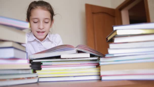 Маленькая девочка в школьной форме читает книгу, сидит между стопками книг — стоковое видео