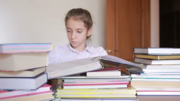 Liten flicka i skoluniform läser en bok, sitter mellan högar av böcker — Stockvideo