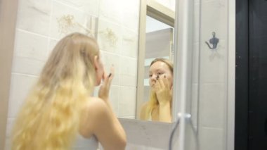 Güzel genç kadın aynanın önünde makyaj yapıyor.