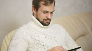 bir tablet ile kanepede ceketli genç sakallı adamı