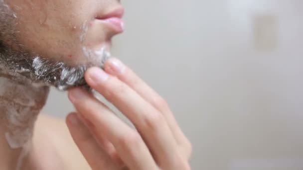 Парень сбривает бороду бритвой в ванной и улыбается — стоковое видео