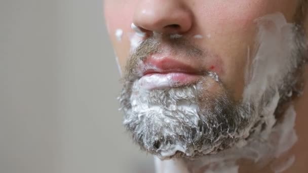 Хлопець голиться з бороди з бритвою у ванній кімнаті і посміхається — стокове відео