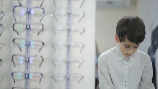 Мальчик-подросток выбирает новые очки в оптике — стоковое видео