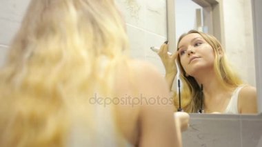 Güzel genç kadın aynanın önünde makyaj yapıyor.