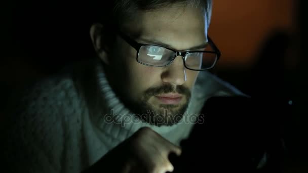 Guy with glasses and a sweater with a tablet in the dark — Stock Video