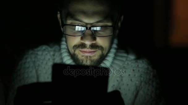 Man met bril en een trui met een tablet in het donker — Stockvideo
