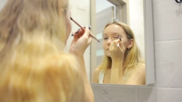 Hermosa joven mujer está haciendo maquillaje delante del espejo . — Vídeos de Stock