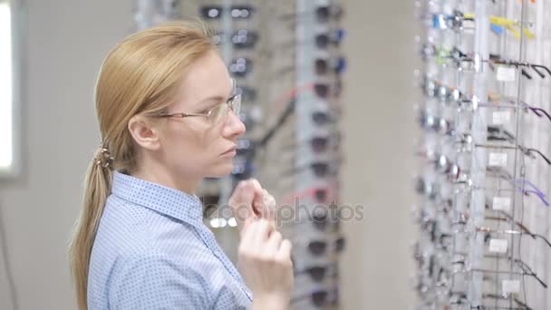 Vrouw blond meisje is het kiezen van nieuwe bril in de optica — Stockvideo