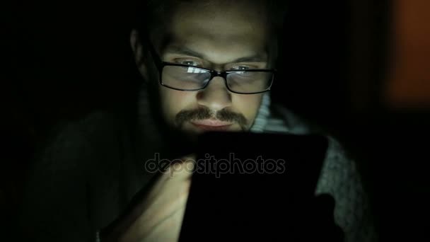 Guy with glasses and a sweater with a tablet in the dark — Stock Video