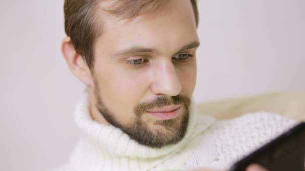 留胡子的年轻人，在一件外套在沙发上用一台平板电脑 — 图库视频影像