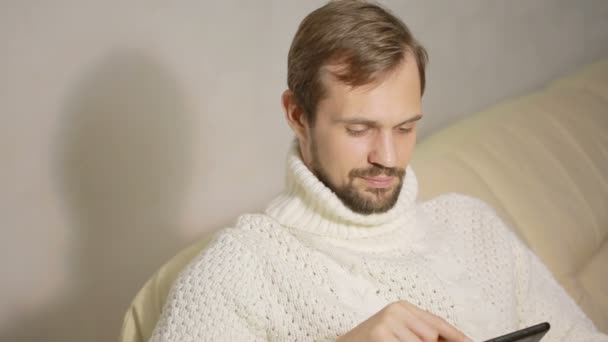 Jeune homme barbu dans une veste sur le canapé avec une tablette — Video