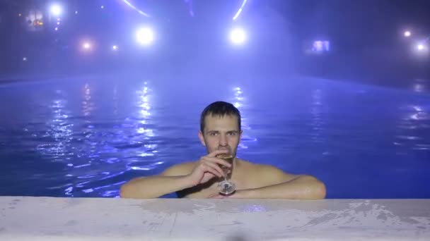 Feliz hombre Nadar en la piscina por la noche y beber de los vasos. Fuente térmica — Vídeo de stock