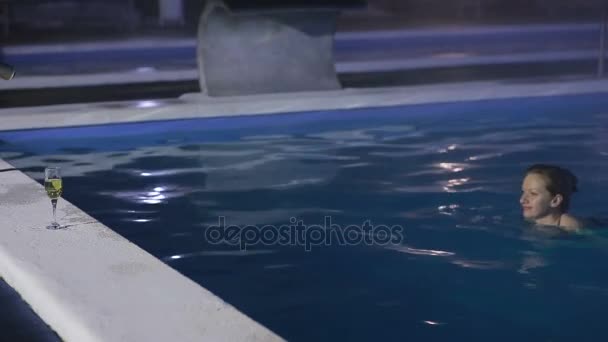 Mujer por la noche en la piscina con agua termal con una copa de champán — Vídeo de stock