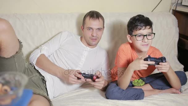 Padre e hijo juegan videojuegos dentro de su casa en el sofá — Vídeos de Stock