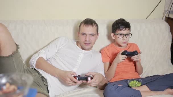 Padre e hijo juegan videojuegos dentro de su casa en el sofá — Vídeos de Stock