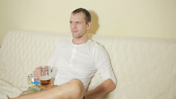 Jovem bebendo cerveja em casa sofá e assistindo televisão — Vídeo de Stock