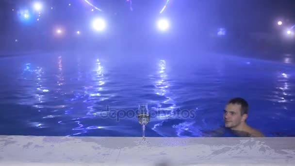 Feliz hombre Nadar en la piscina por la noche y beber de los vasos. Fuente térmica — Vídeo de stock