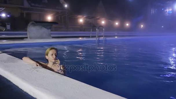 Mujer por la noche en la piscina con agua termal con una copa de champán — Vídeo de stock