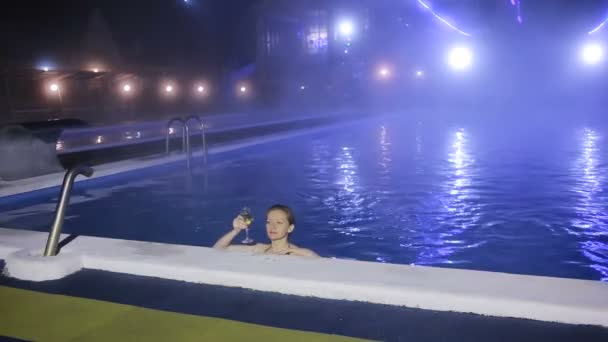 Mujer por la noche en la piscina con agua termal con una copa de champán — Vídeo de stock