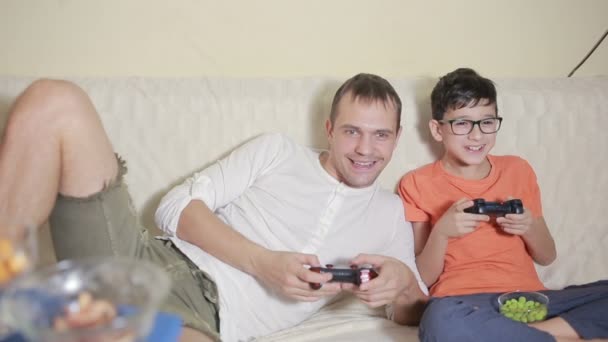 Πατέρας και γιος παιχνίδι βίντεο μέσα στο σπίτι τους στον καναπέ — Αρχείο Βίντεο