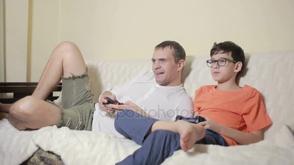 Vater und Sohn spielen Videospiel in ihrem Haus auf der Couch — Stockvideo