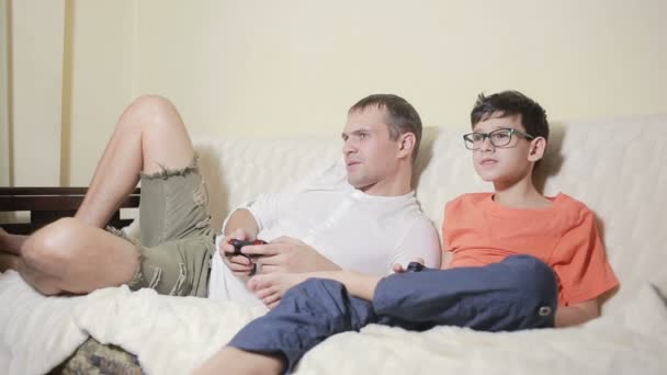 Vater und Sohn spielen Videospiel in ihrem Haus auf der Couch — Stockvideo