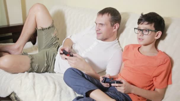 Padre e hijo juegan videojuegos dentro de su casa en el sofá — Vídeos de Stock