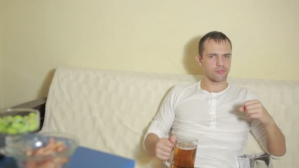 Νεαρός πίνοντας μπύρα στο σπίτι καναπέ και βλέποντας τηλεόραση — Αρχείο Βίντεο