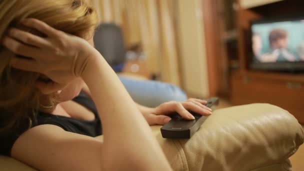 Hermosa mujer viendo la televisión sentada en el sofá en casa, cambia de canal — Vídeo de stock