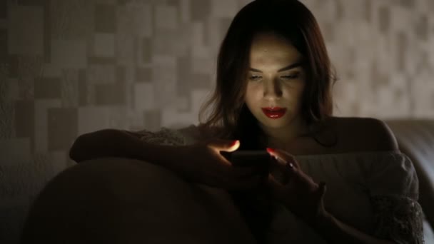 Kobieta z telefonem w ciemności w domu na kanapie. telefon odbicie twarzy — Wideo stockowe