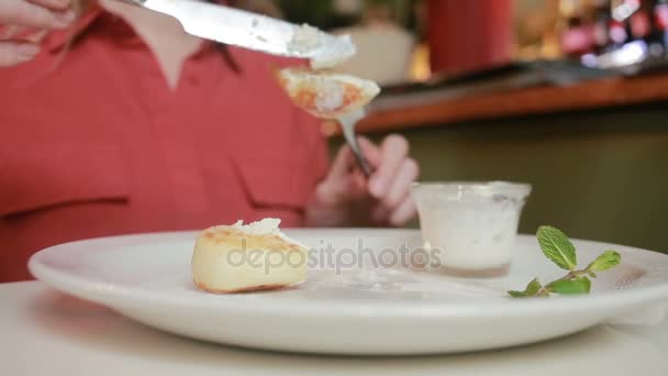 La chica en el café comiendo panqueques de queso con tenedor de crema agria y cuchillo . — Vídeos de Stock