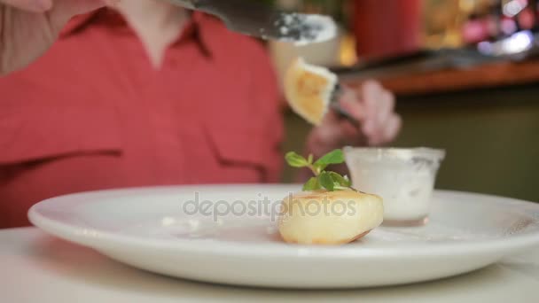 Flickan i café äta ost pannkakor med gräddfil gaffel och kniv. — Stockvideo