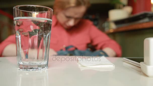 Chica en la cafetería está buscando algo en una bolsa sobre un fondo de vidrio con agua — Vídeo de stock