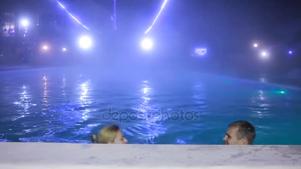 Pareja hombre y mujer nadando en una piscina con agua termal por la noche . — Vídeo de stock