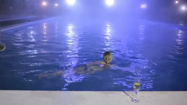 Жінка вночі в басейні з теплою водою зі склянкою шампанського — стокове відео