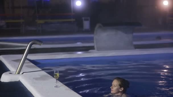 Mujer por la noche en la piscina con agua termal con una copa de champán — Vídeos de Stock
