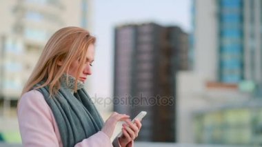 kız pembe bir ceket telefon ile modern bir şehir üzerinde yürür. gökdelenlerin arka plan