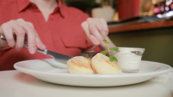 Flickan i café äta ost pannkakor med gräddfil gaffel och kniv. — Stockvideo