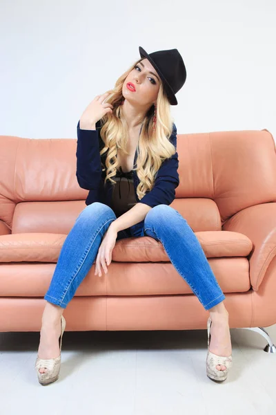 Hermosa rubia en sombrero una lencería y jeans. sentado en el sofá — Foto de Stock