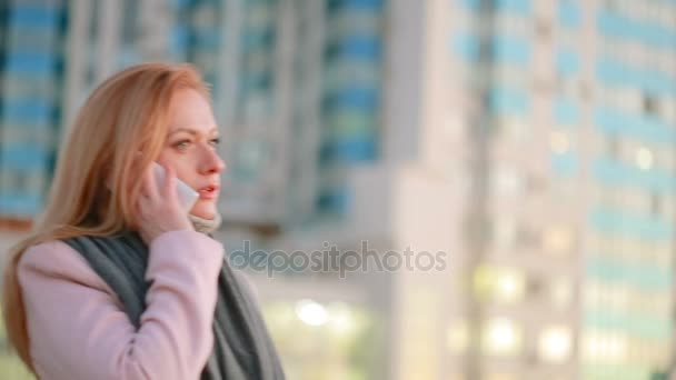 Fille dans un manteau rose avec téléphone marche sur une ville moderne. fond de gratte-ciel — Video