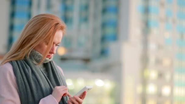 Fille dans un manteau rose avec téléphone marche sur une ville moderne. fond de gratte-ciel — Video