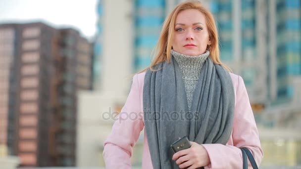 Chica en un abrigo rosa con paseos telefónicos en una ciudad moderna. fondo de rascacielos — Vídeos de Stock