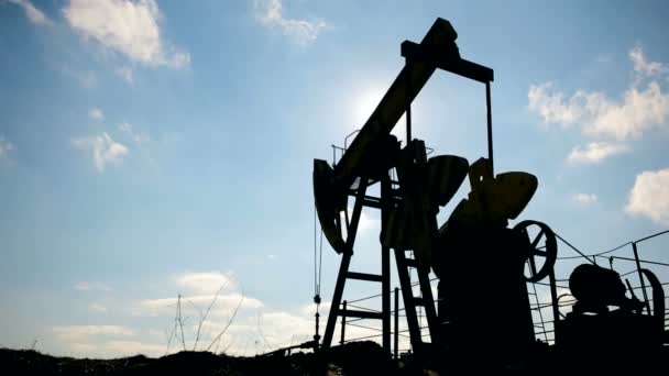 Silhouette of working oil pump on a background of blue sky and white clouds. — Stock Video