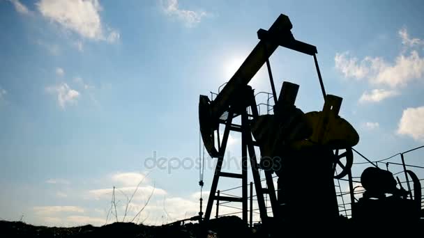 Silhouette of working oil pump on a background of blue sky and white clouds. — Stock Video