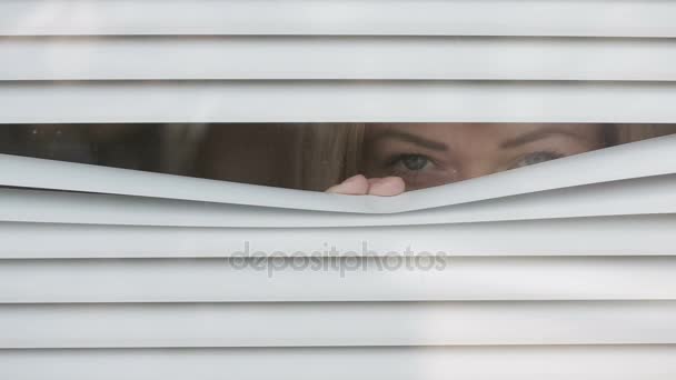 Una donna che guarda fuori dalla finestra attraverso le tende verso la strada, spiando. Sospettato — Video Stock