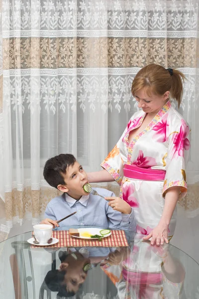 Joven feliz hermosa madre y su hijo comiendo desayuno saludable — Foto de Stock