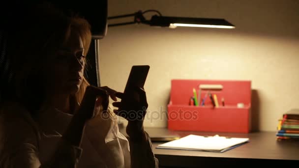 Žena sedí v kanceláři na stůl a psal zprávy na smartphone. — Stock video