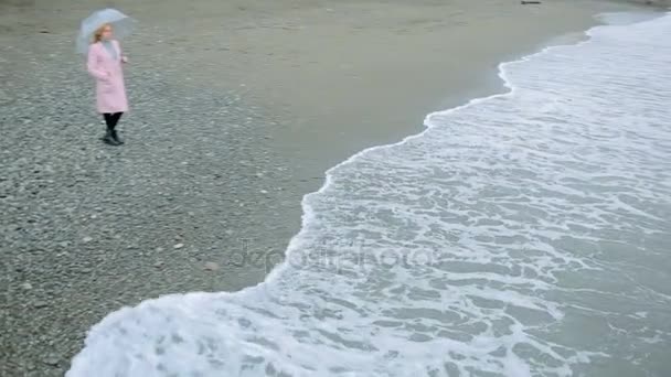 嵐の中の海によって透明傘のピンクのコートの女の子. — ストック動画